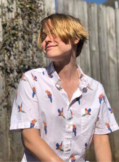 Author Dev Jannerson, a person with pale complexion and short blonde hair, in a white, short-sleeved button-down with a colorful parrot pattern